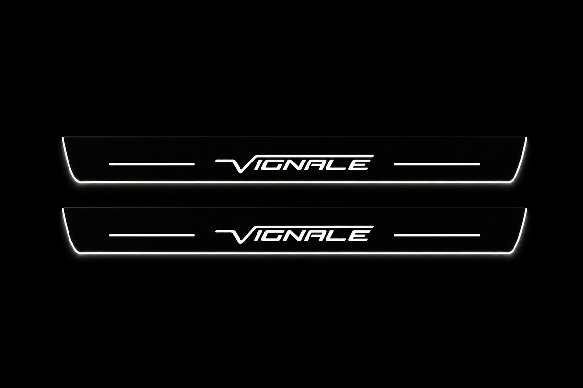 Product visualization: two exact Mondeo Vignale front plates, slender original outline and logo; black main hidden metal/white LED, white secondary visible silver flat brushed stainless steel door sill plates with white LED artwork and edges, dark background.