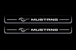 Product visualization: two exact mustang-pony-legacy flat Stainless front sill plates with original artwork, neutral white LEDs and own thin-edge geometry flat brushed stainless steel door sill plates with white LED artwork and edges, dark background.