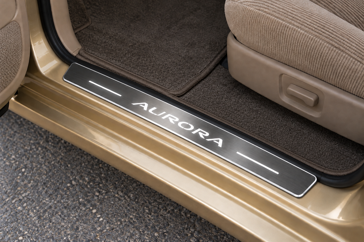 Oldsmobile Aurora Stainless sill visualization directly against the black rubber seal on exposed gold metal, AURORA lettering, two white bars and thin edge illumination.