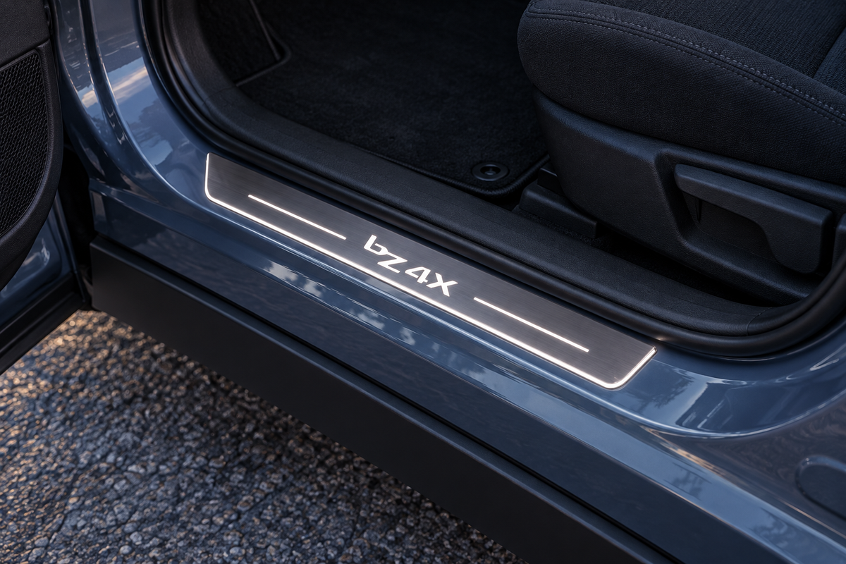 Product visualization of a brushed stainless bZ4X sill with white lettering, narrow light bars and edge lighting in a blue-grey Toyota doorway.