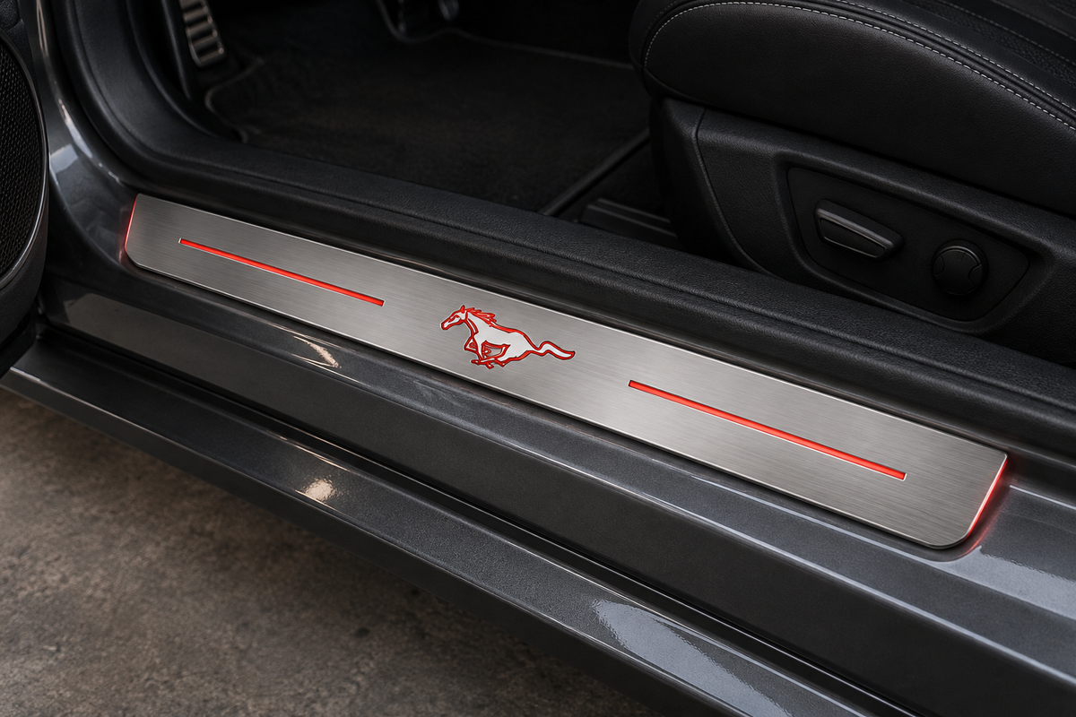 Product visualization of a brushed stainless steel Mustang door sill with red running-horse outline, two light bars and restrained side-edge light in a doorway; not a customer installation.