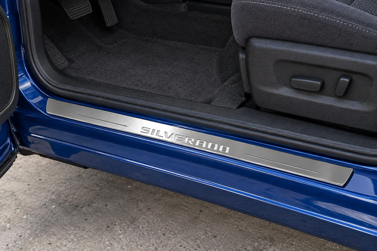 Product visualization of an unlit brushed stainless SILVERADO sill on a blue truck’s painted-metal threshold.