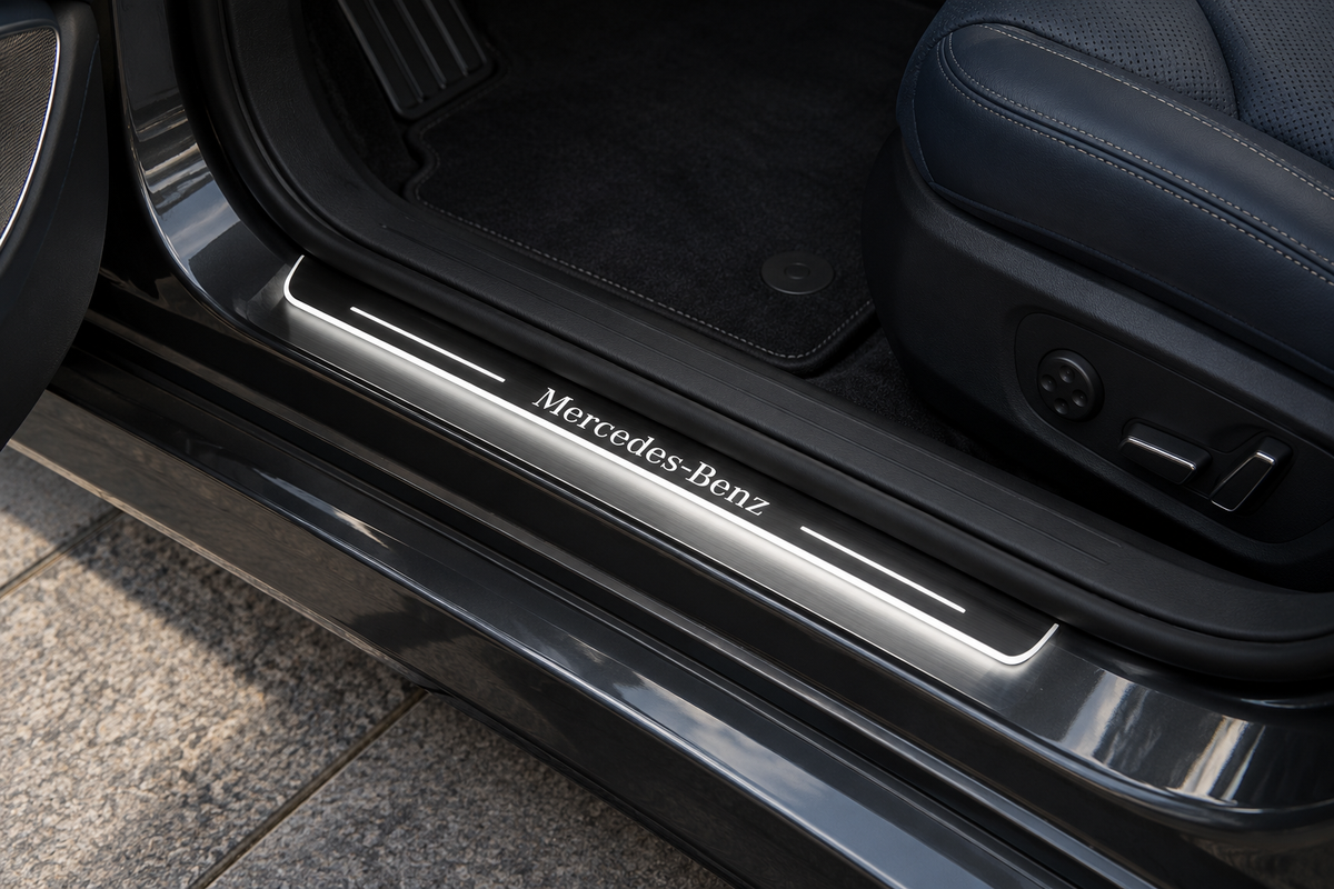 Product visualization of a grey stainless Mercedes-Benz-lettering sill with white light bars and edge on a dark sedan threshold beside navy leather.
