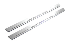 Two long silver-finished door sill plates with Land Cruiser Prado lettering on a light background, angled view.