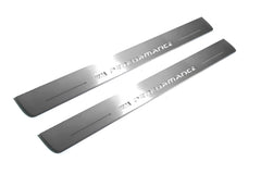 Two long silver-finished door sill plates with M Performance lettering on a light background, angled view.