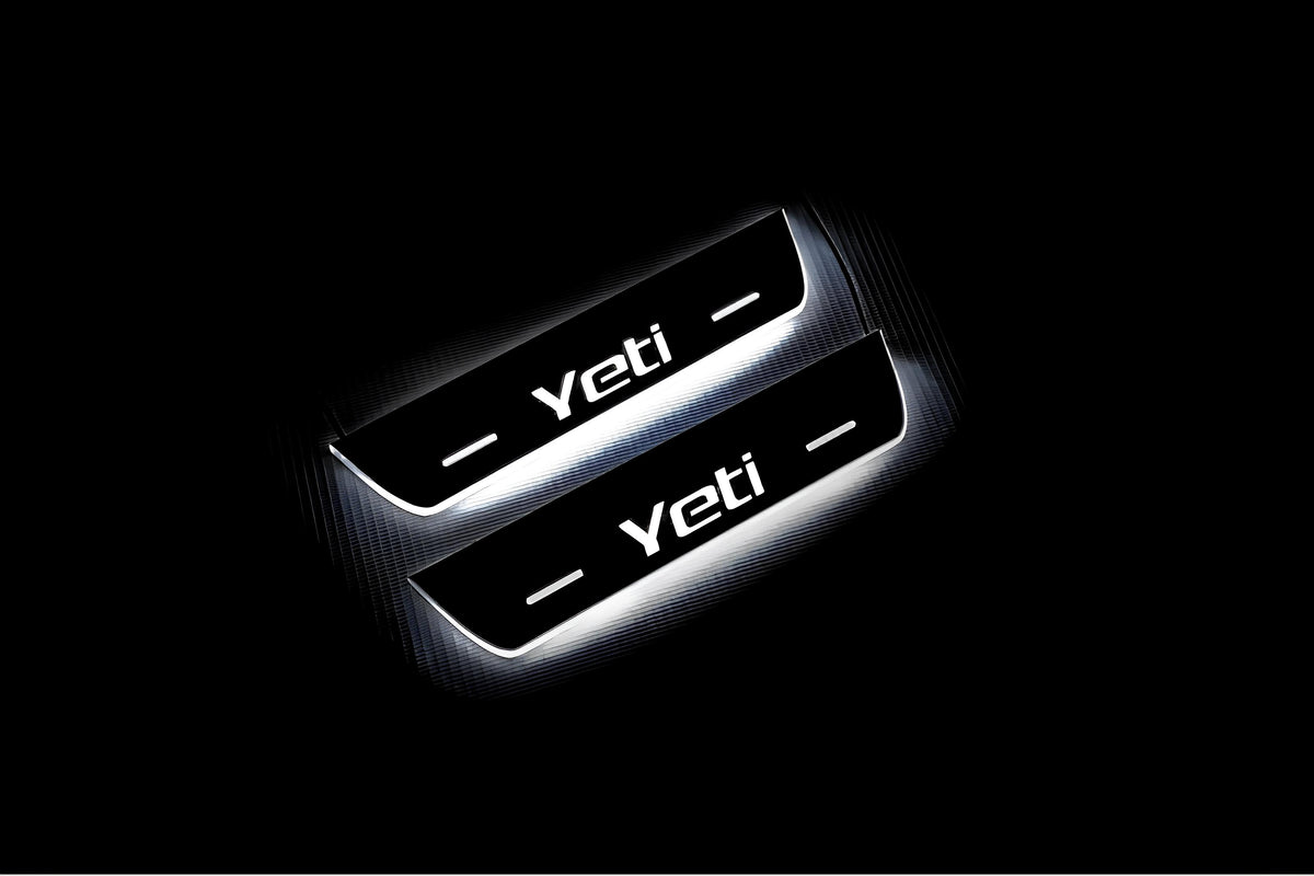 Two short door sill plates with Yeti lettering and edges illuminated in white, angled view on a dark background.