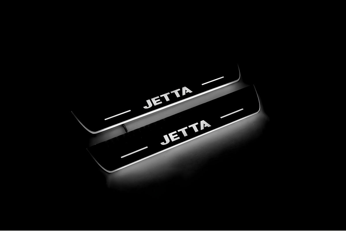 Two short door sill plates with Jetta lettering and edges illuminated in white, angled view on a dark background.
