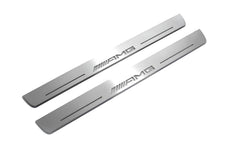 Two long silver-finished door sill plates with AMG lettering on a light background, angled view.