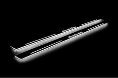 Two long door sill plates with Mercedes-Benz lettering and edges illuminated in white, angled view on a dark background.