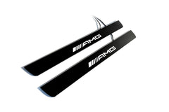 Two black door sill plates with white AMG lettering and visible wiring, photographed on a light background.