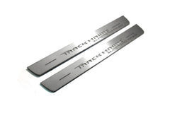 Two long silver-finished door sill plates with Trackhawk Supercharged lettering on a light background, angled view.
