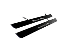 Two black door sill plates with white Mercedes-Benz lettering and visible wiring, photographed on a light background.