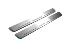 Two long silver-finished door sill plates with AMG lettering on a light background, angled view.