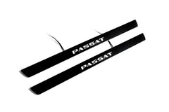 Two black door sill plates with white Passat lettering and visible wiring on a light background.