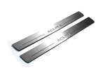 Two long silver-finished door sill plates with Acura lettering on a light background, angled view.