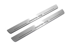 Two long silver-finished door sill plates with AMG lettering on a light background, angled view.