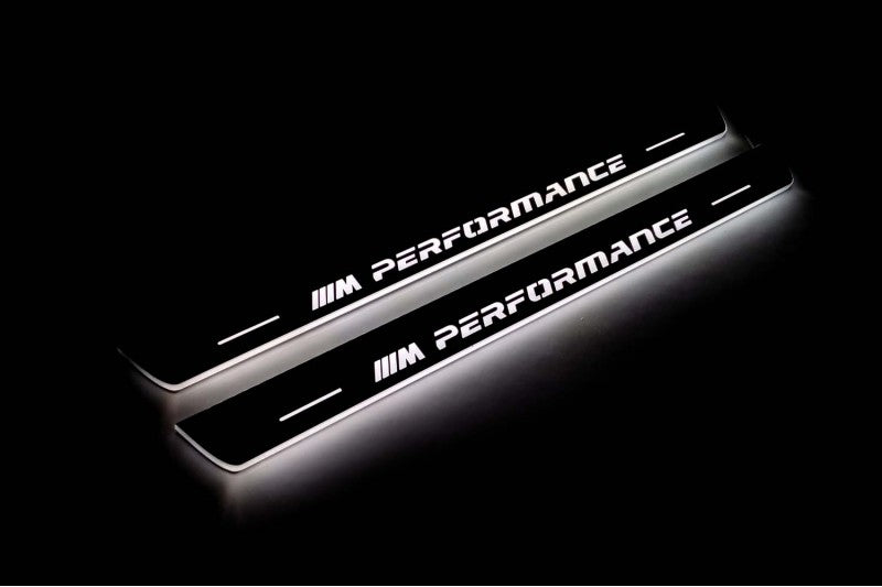 Two long door sill plates with M Performance lettering and edges illuminated in white, angled view on a dark background.