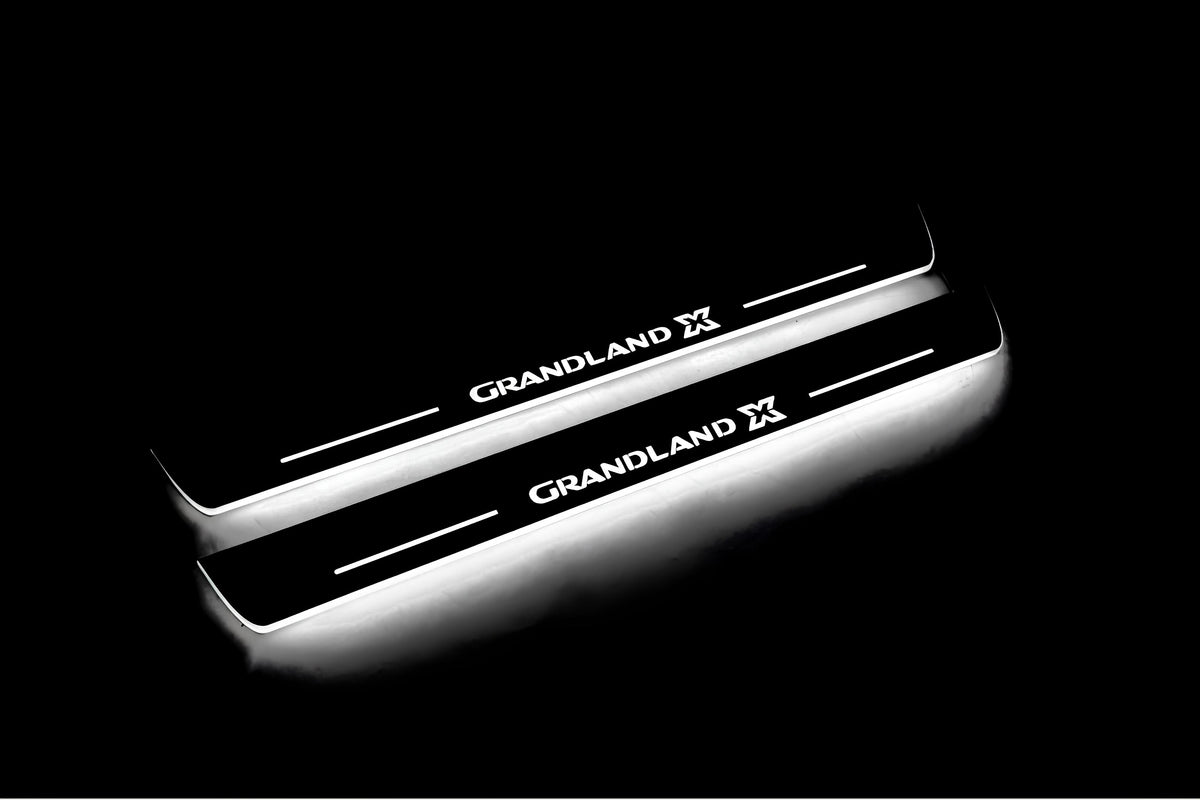 Two long door sill plates with Grandland X lettering and edges illuminated in white, angled view on a dark background.