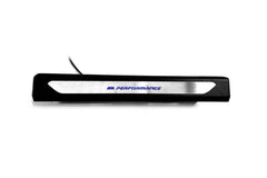 Black molded threshold trim with a silver insert bearing blue M Performance lettering, straight-on view.