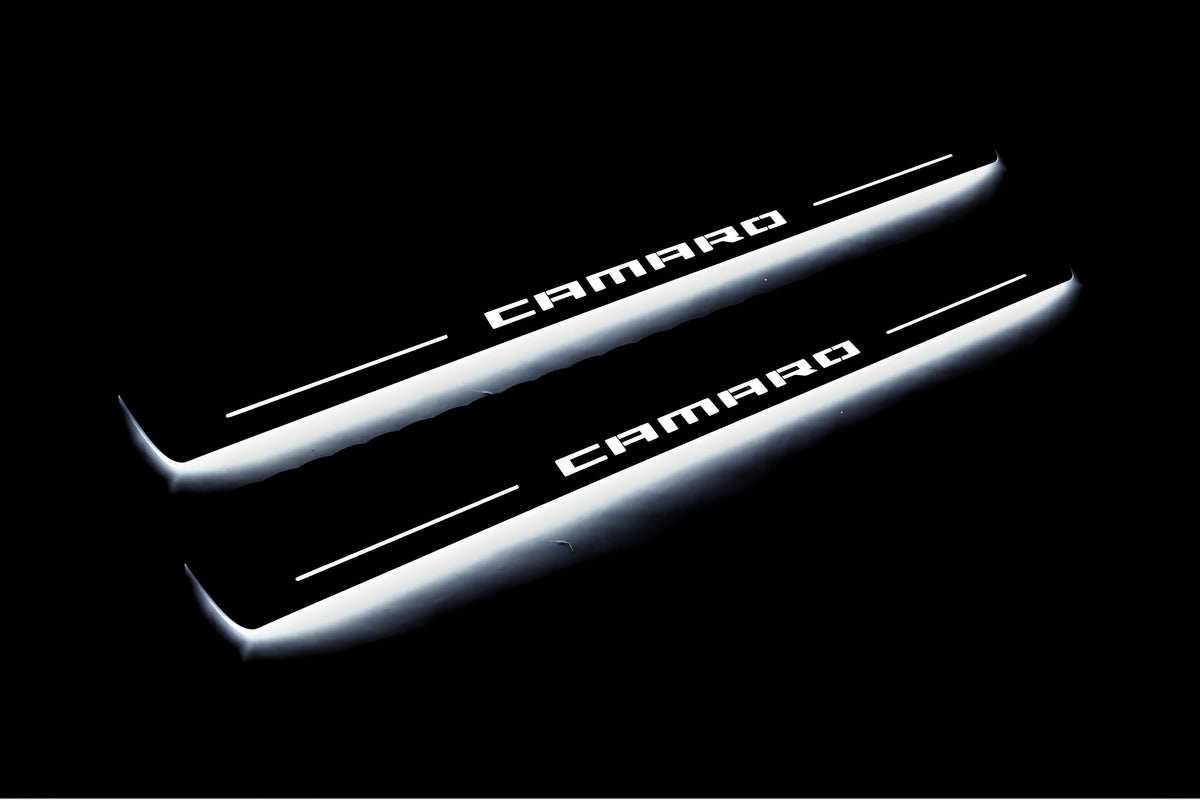 Two long door sill plates with Camaro lettering and edges illuminated in white, angled view on a dark background.