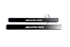 Two black door sill plates with white AMG lettering and visible wiring, photographed on a light background.
