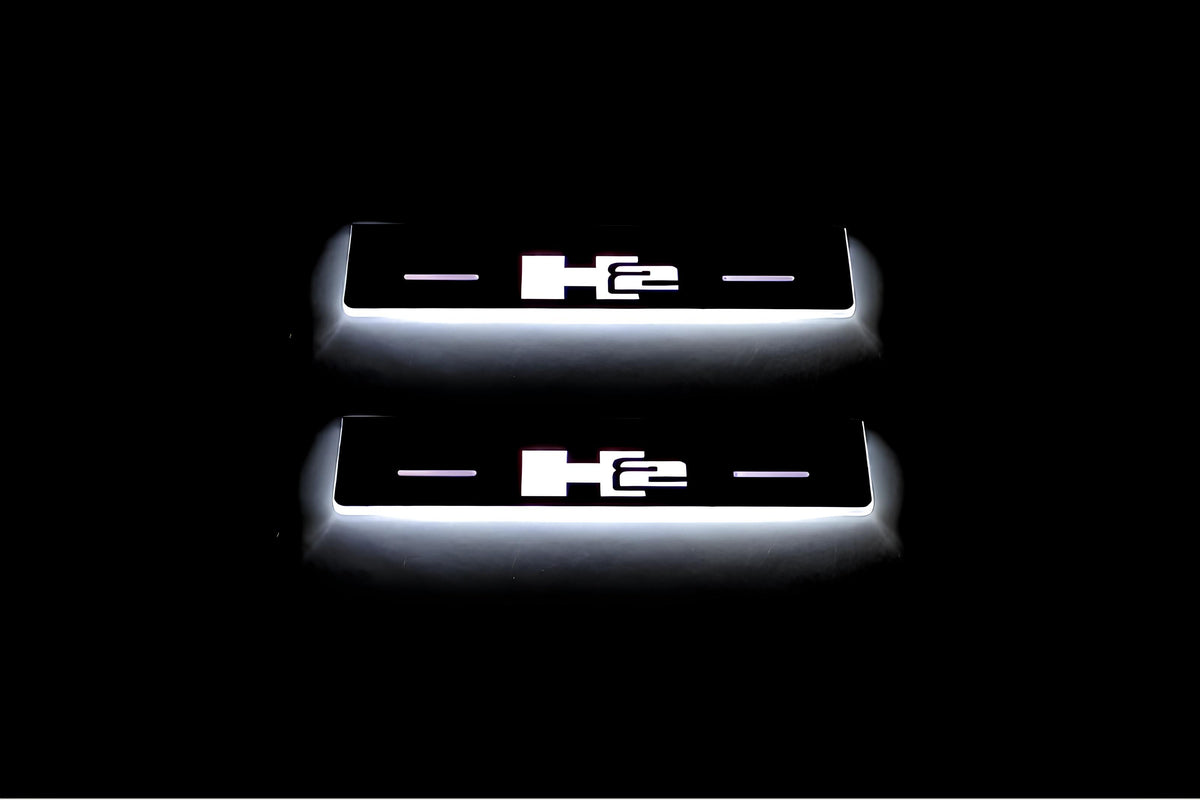 Two short door sill plates with H2 lettering and edges illuminated in white, straight-on view on a dark background.