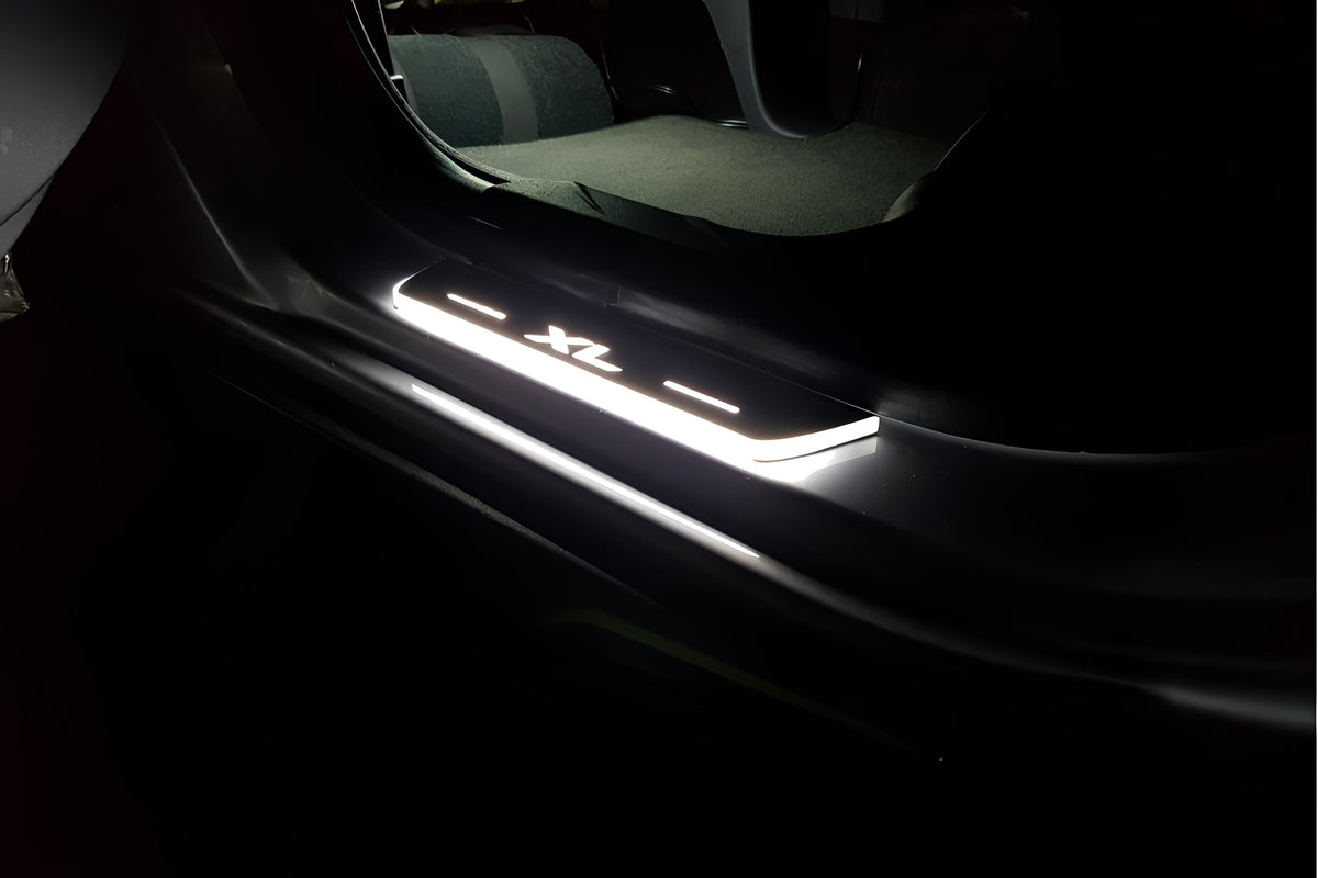 Short door sill with illuminated XL lettering fitted beside a vehicle rear seat; installation example.