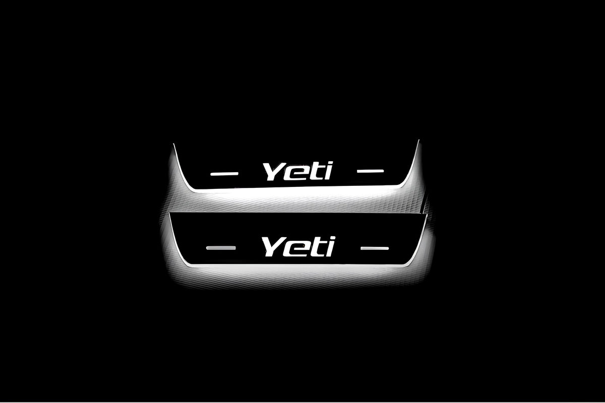 Two short door sill plates with Yeti lettering and edges illuminated in white, straight-on view on a dark background.