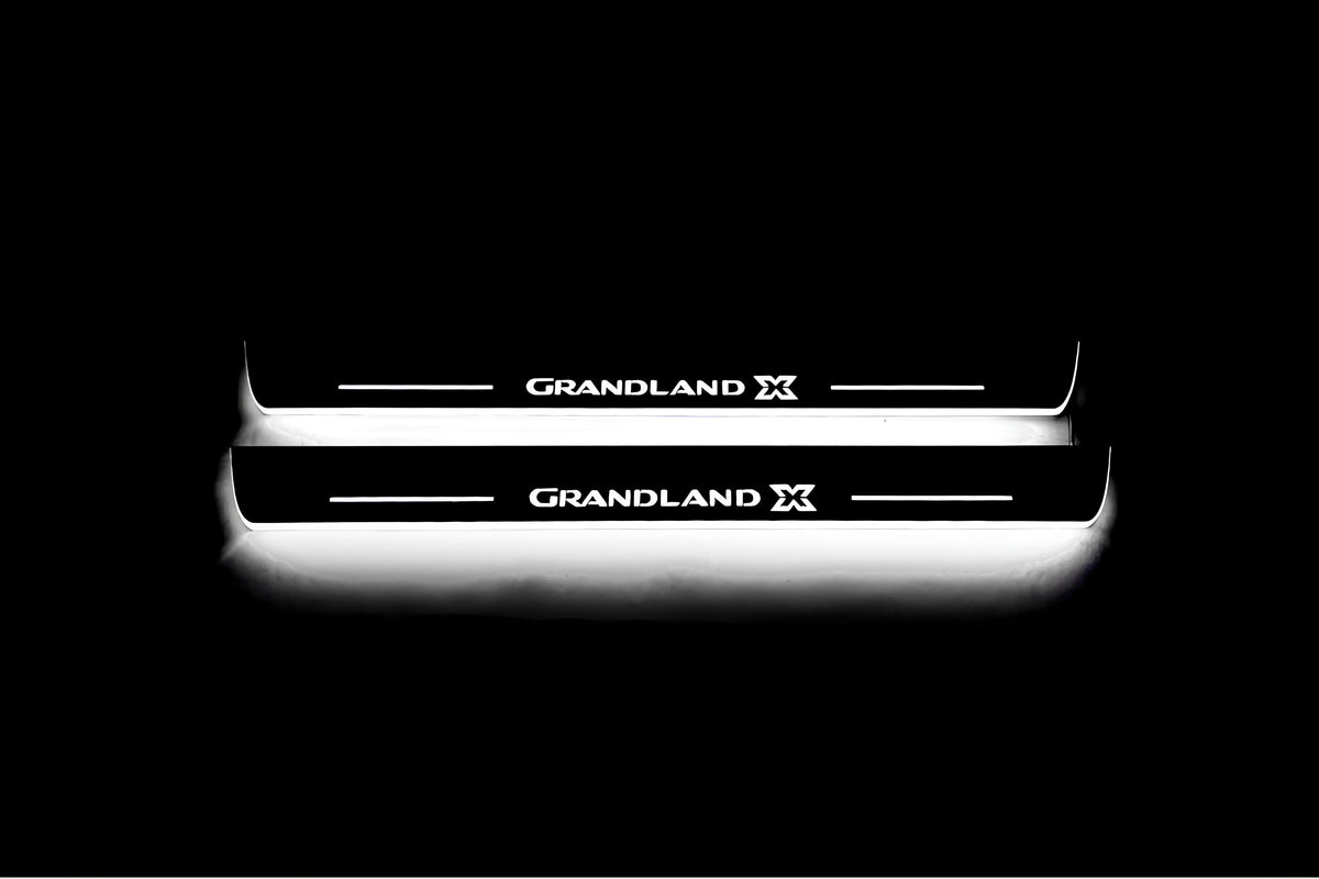 Two long door sill plates with Grandland X lettering and edges illuminated in white, straight-on view on a dark background.
