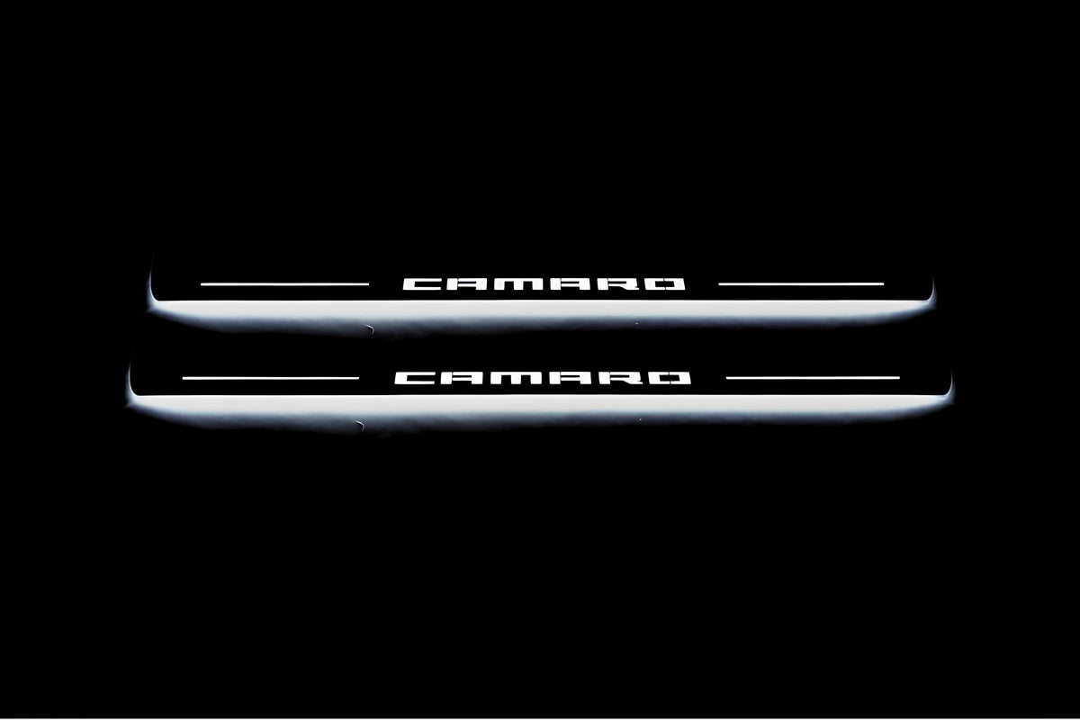 Two long door sill plates with Camaro lettering and edges illuminated in white, straight-on view on a dark background.