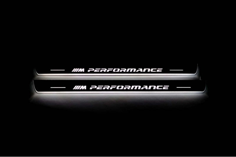 Two long door sill plates with M Performance lettering and edges illuminated in white, straight-on view on a dark background.