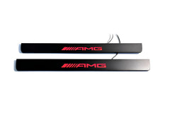 Two black door sill plates with red AMG lettering and visible wiring, photographed on a light background.