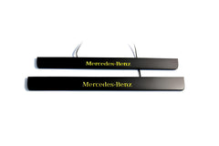 Two black door sill plates with yellow Mercedes-Benz lettering and visible wiring, photographed on a light background.