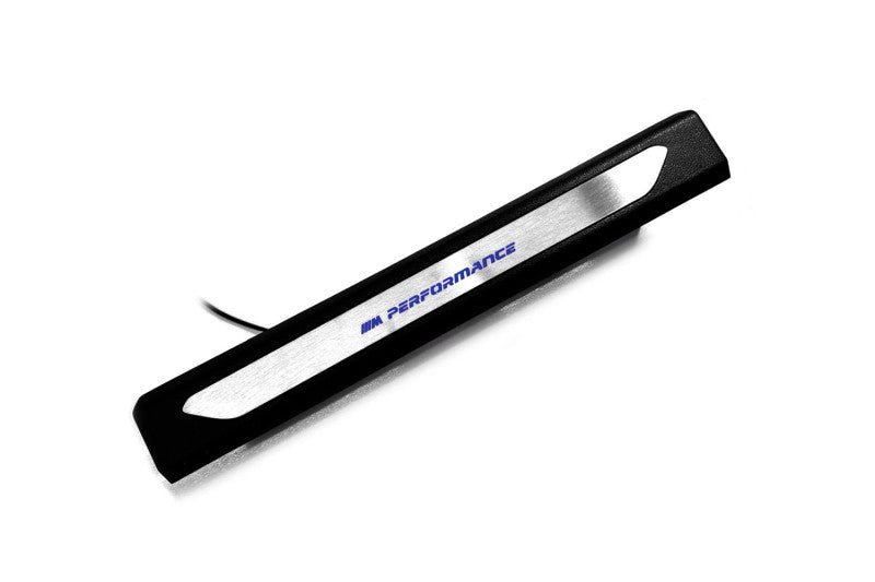 Black molded threshold trim with a silver insert bearing blue M Performance lettering and an attached wire, angled view.