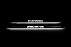 Two long door sill plates with Transformers lettering and edges illuminated in white, straight-on view on a dark background.