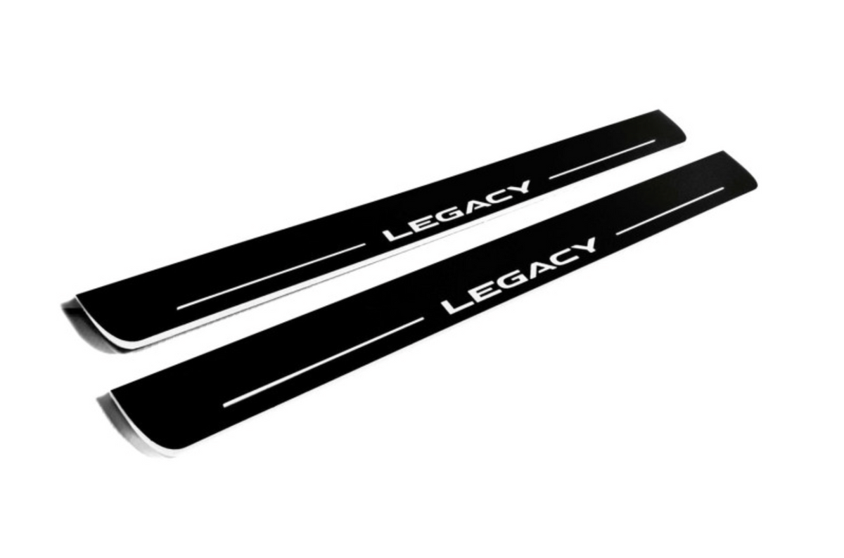 Two long black-finished door sill plates with white Legacy lettering and horizontal lines, angled view on a white background.