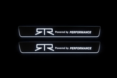 Two door sill plates with RTR emblems, Powered by PERFORMANCE lettering and outlined edges illuminated white on a dark background.