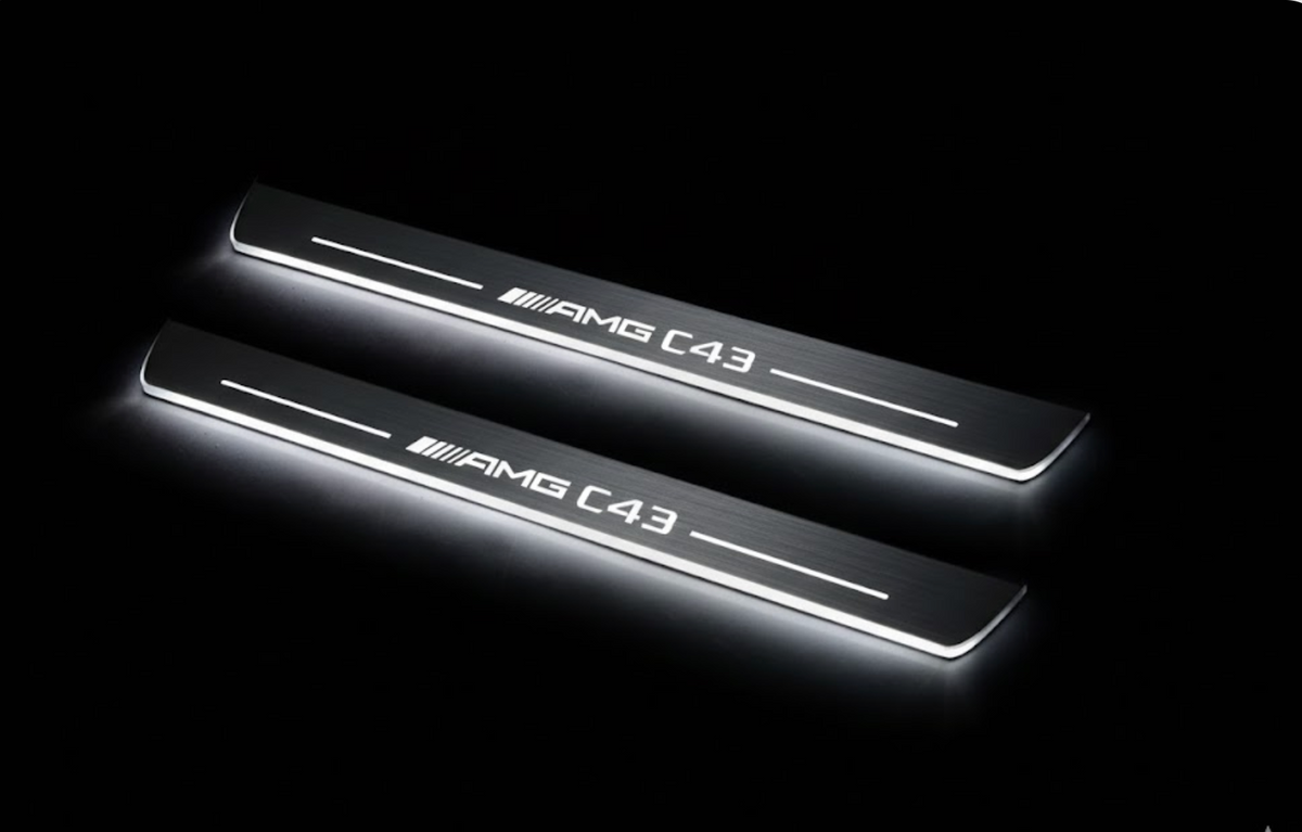 Two long door sill plates with AMG C43 lettering and edges illuminated in white, angled view on a dark background.