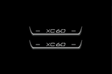 Two short door sill plates with XC60 lettering and edges illuminated in white, straight-on view on a dark background.