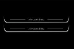 Two long door sill plates with Mercedes-Benz lettering and edges illuminated in white, straight-on view on a dark background.