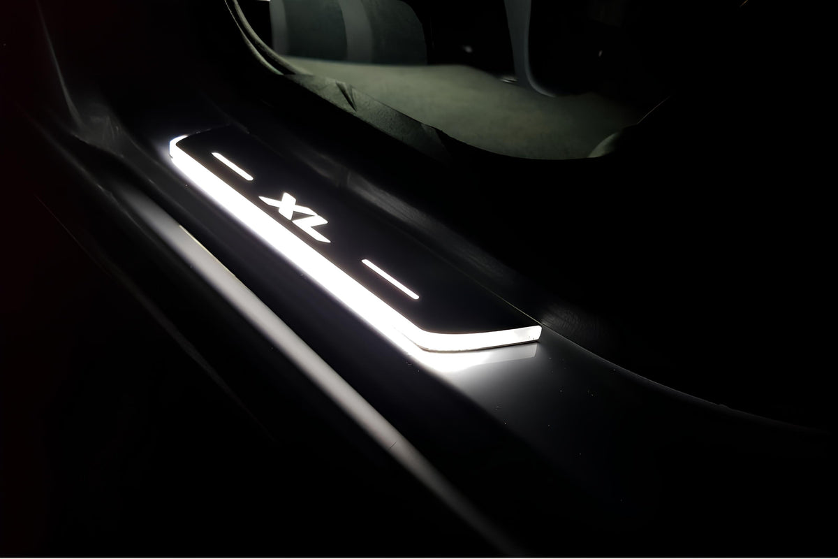 Short door sill with illuminated XL lettering fitted beside a vehicle rear seat; installation example.