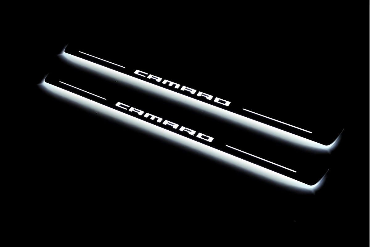 Two long door sill plates with Camaro lettering and edges illuminated in white, angled view on a dark background.