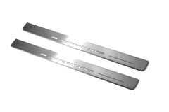 Two long silver-finished door sill plates with M Performance lettering on a light background, angled view.