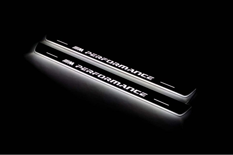 Two long door sill plates with M Performance lettering and edges illuminated in white, angled view on a dark background.