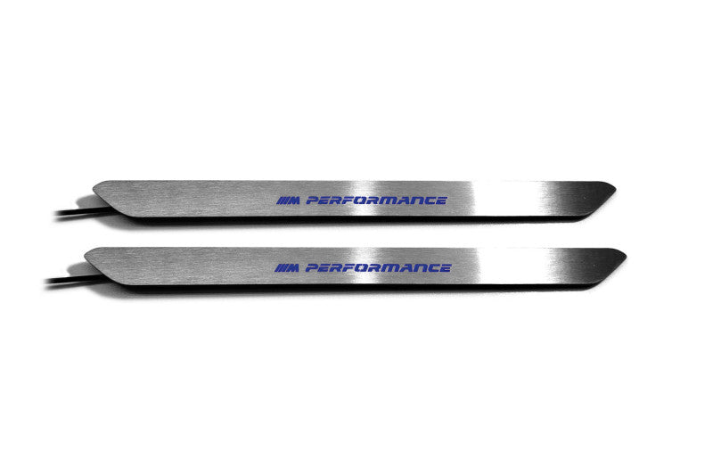 Two narrow silver door sill inserts with blue M Performance lettering and attached wires, straight-on view on a white background.
