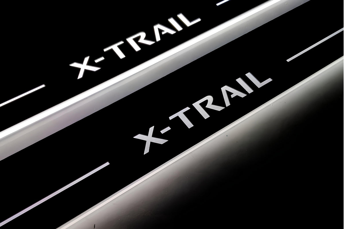 Close-up of X-Trail lettering and illuminated edges on door sill plates against a dark background.