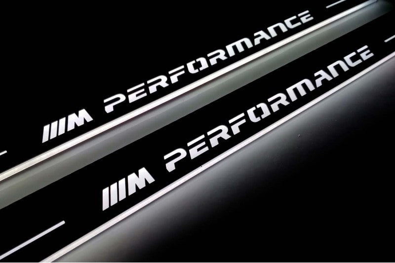 Close-up of M Performance lettering and illuminated edges on door sill plates against a dark background.