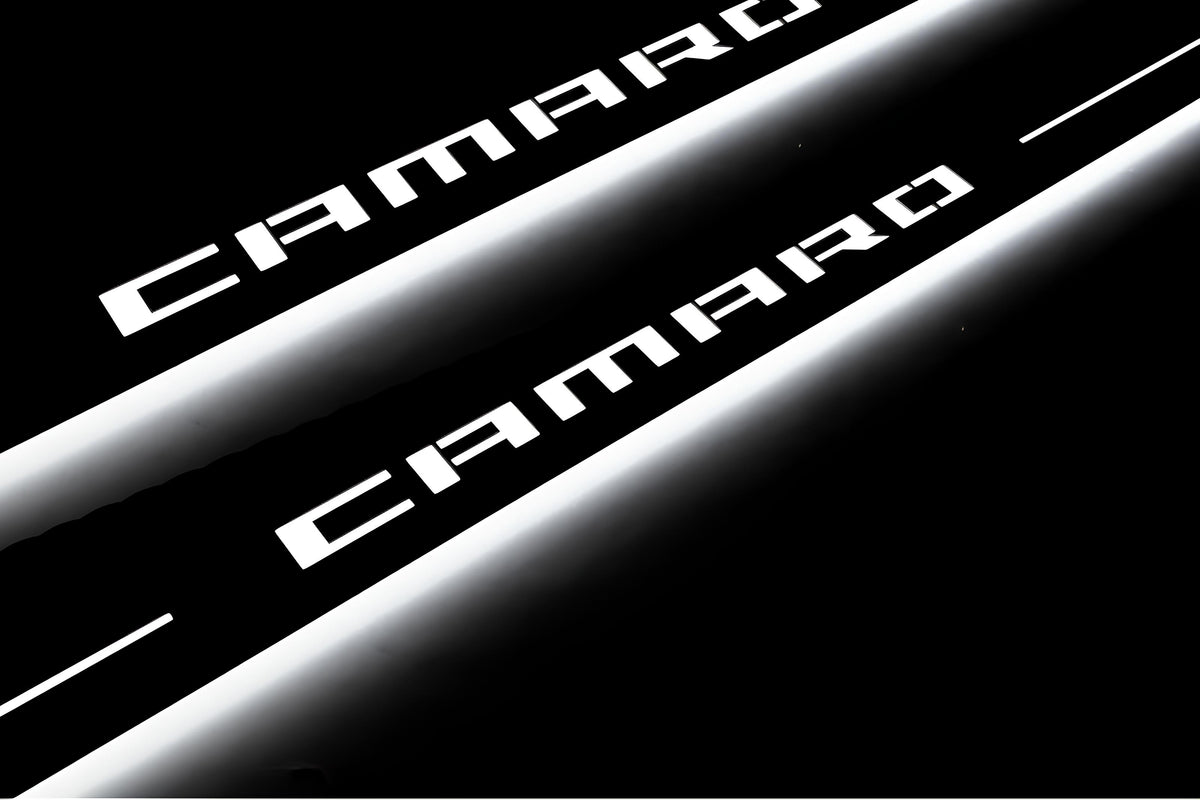Close-up of Camaro lettering and illuminated edges on door sill plates against a dark background.