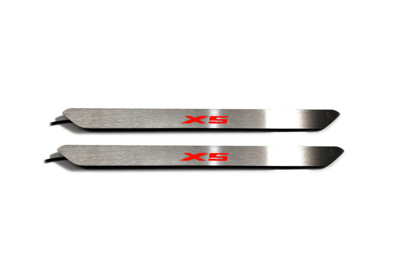 Two narrow silver door sill inserts with red X5 lettering and attached wires, straight-on view on a white background.