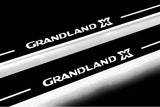 Close-up of Grandland X lettering and illuminated edges on door sill plates against a dark background.